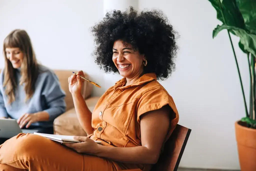 Black businesswoman smiling cheerfully while sitting in a meeting with her colleague. Happy young businesswomen working together in a modern workplace.